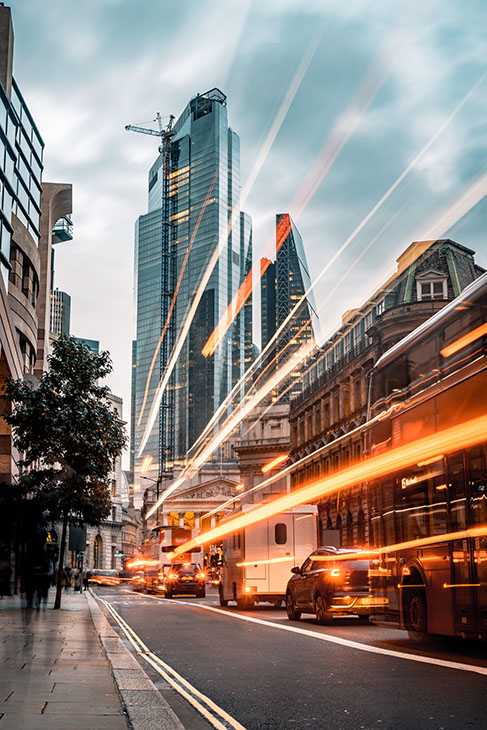 Long exposure photo with evening illumination at Queen Victoria street towards Stock Exchange in London city during blue hour on a cloudy English evening. Crowd and traffic with motion blur due to the exposure time with unrecognisable accidental commuters and tourist. Vertical image with copy space and it is ideal for business conceptual background. Shot on Canon EOS R full frame system. Toned image.