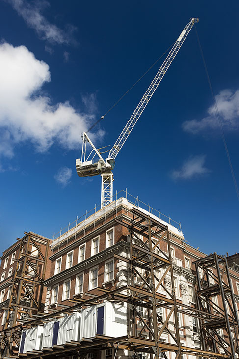 Renovation of red brick building with crane and scaffolding. Material storage containers.